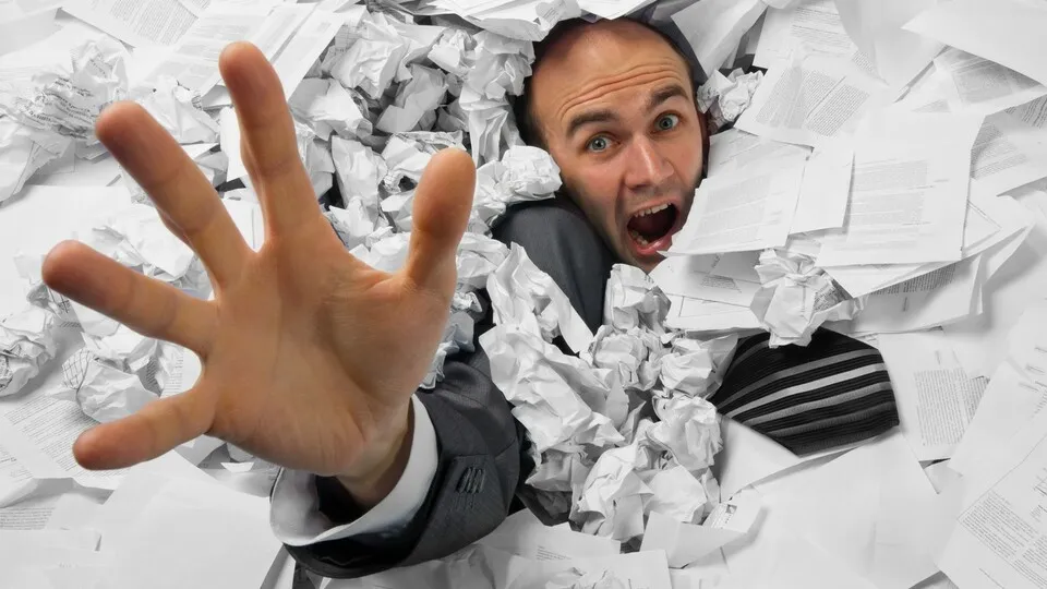 Businessman sinking in heap of documents and asking for help